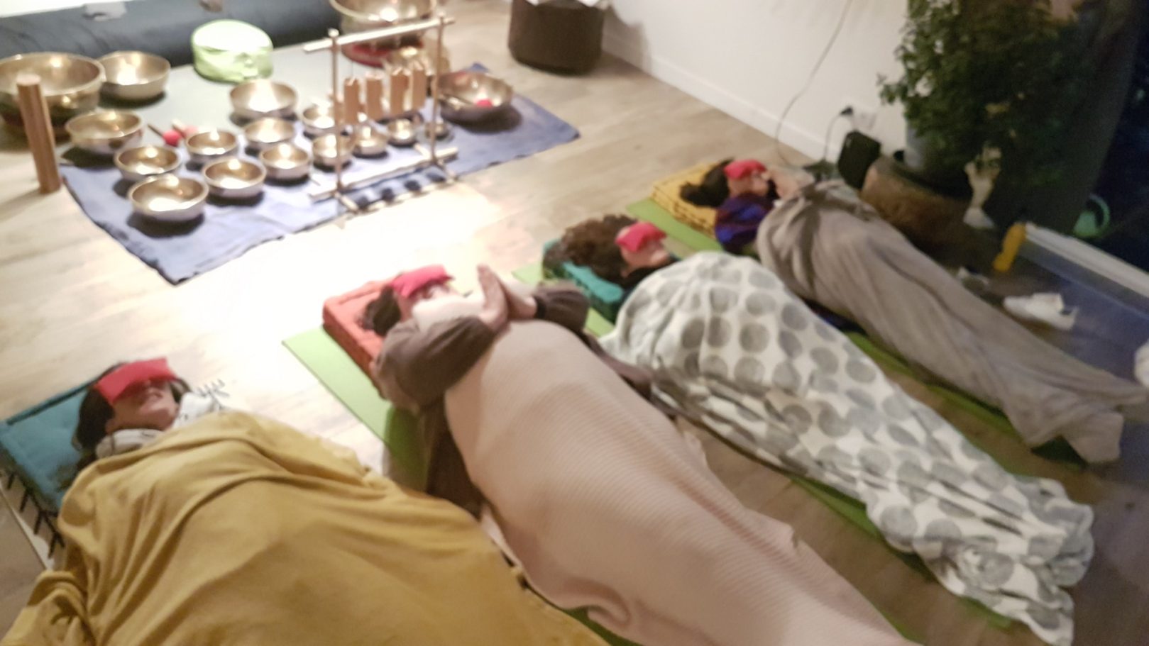 Plusieurs personnes allongées sous des couvertures, les yeux couverts, en relaxation sonore après une séance de bols tibétains.

