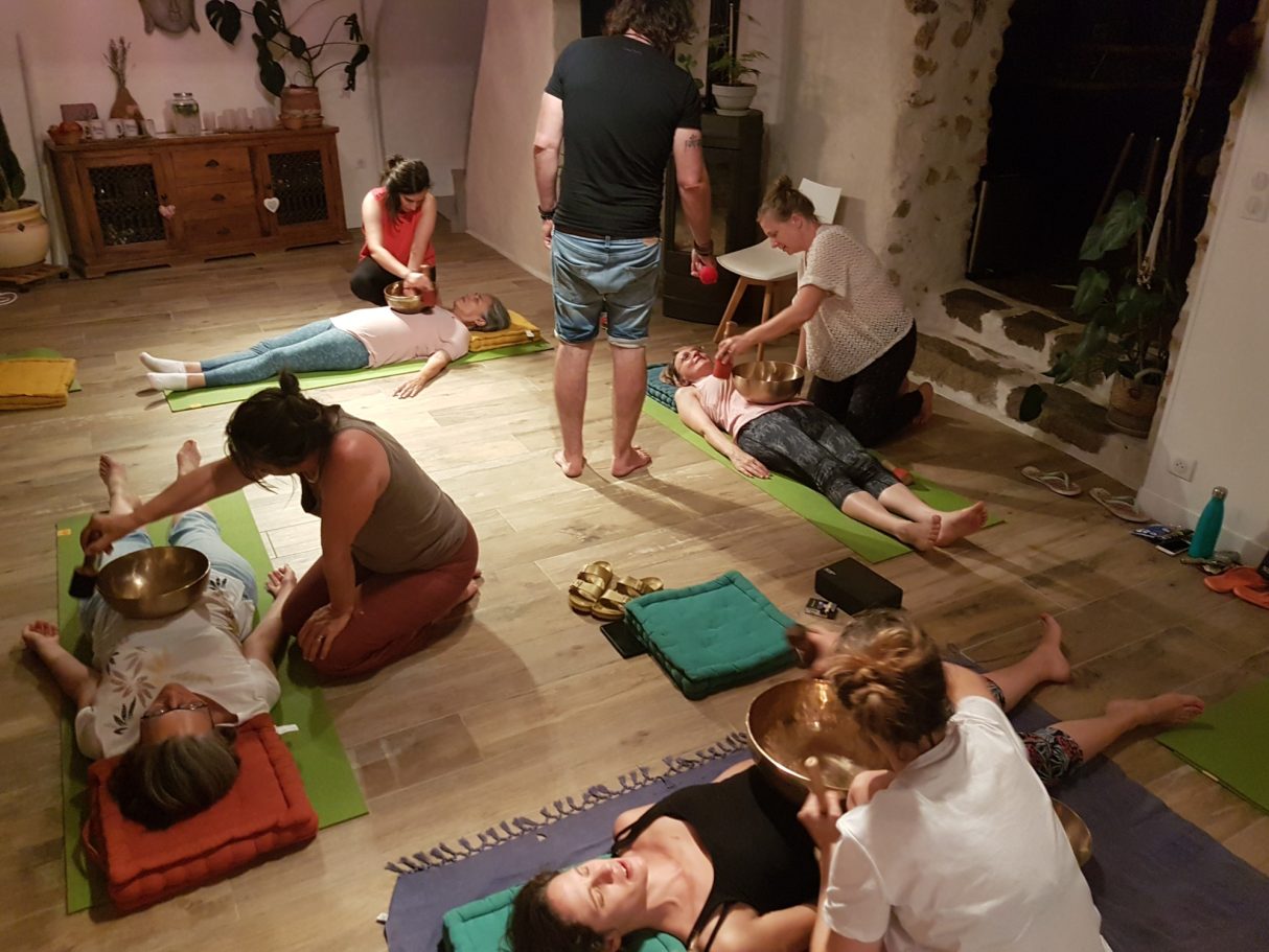 Plusieurs participants en binômes pratiquent des soins vibratoires avec des bols tibétains posés sur le corps de personnes allongées.