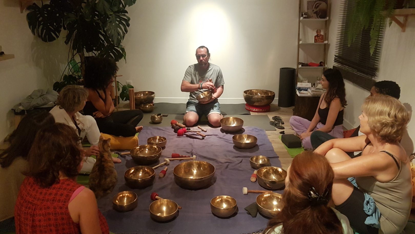  Cercle chaleureux de participants réunis autour de bols chantants tibétains et de maillets, dans une ambiance douce, accompagnés même d’un 